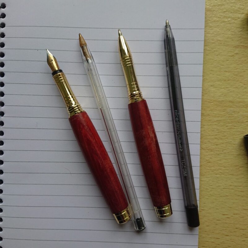 Two pen set made from walnut with broader, wider bodies, though standard width, but shaped grip area. The pens are handmade. This shows the pens compared to two normal everyday type pens