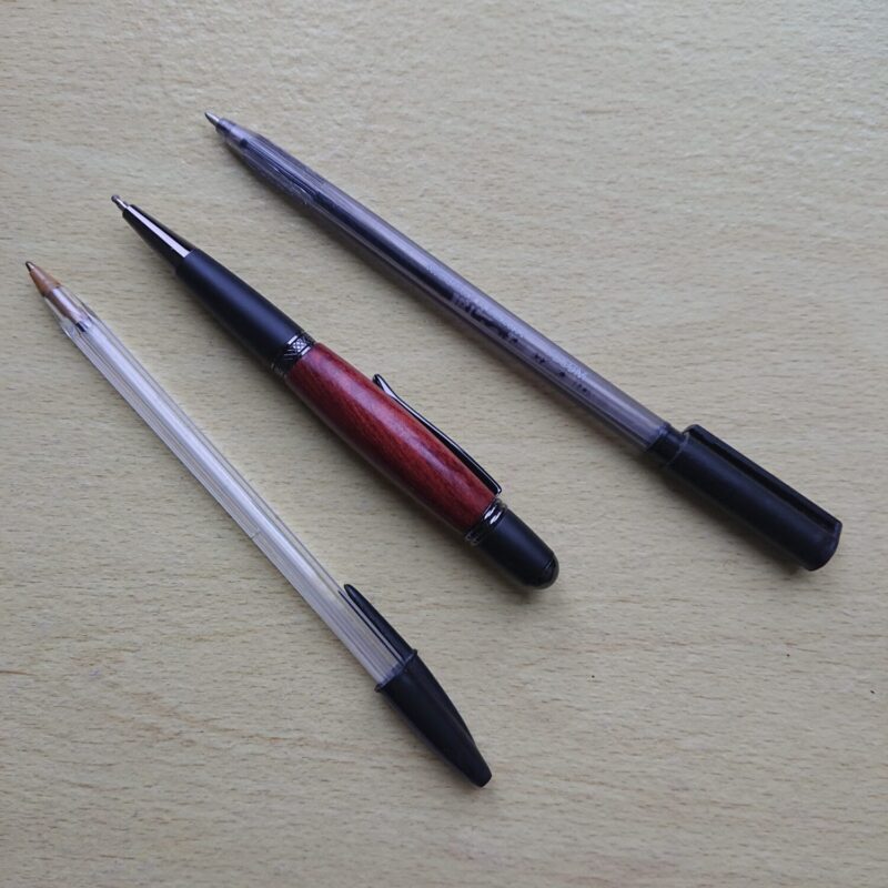 Mahogany handmade wooden pen with wider body and black styling. Retractable tip. A comparison between the broad pen and two everyday type pens.