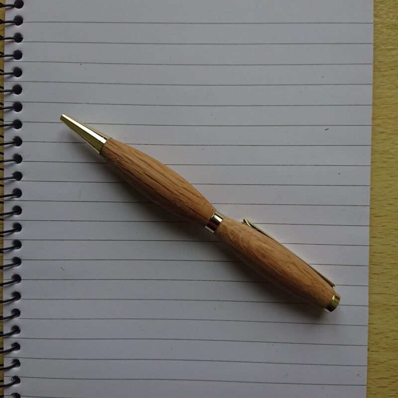 oak handmade pen with wider grip, but narrow waist resting on lined paper. The pen has a retractable tip.